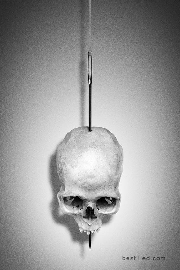 Skull impaled on a needle hanging by a thread. Surreal black and white art by Joseph Westrupp.
