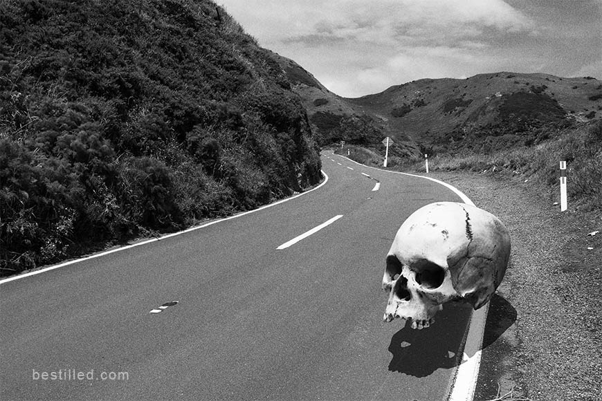 Giant skull floating over a country road in New Zealand, surreal art in black and white by Joseph Westrupp.