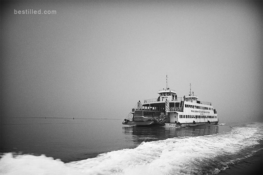 Art photograph of a ferry in Vietnam, with a line of wake from another boat, by Joseph Westrupp.