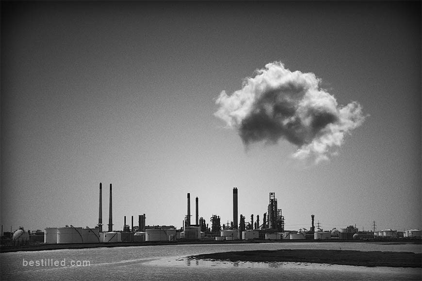 Surreal black and white art photograph of Coryton Refinery, England, under a single cloud. By Joseph Westrupp.